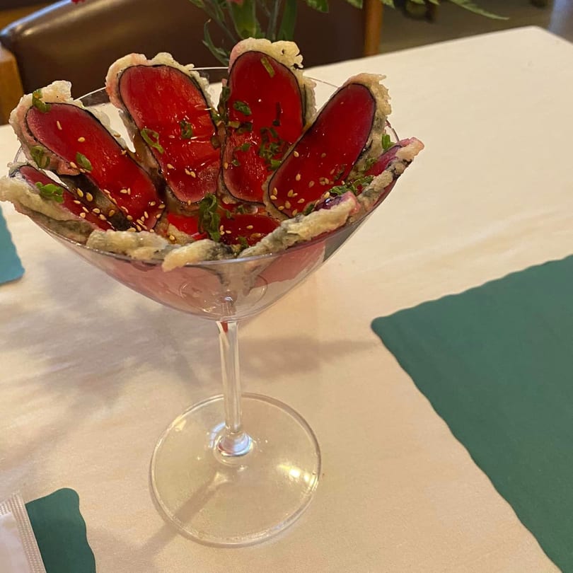 Tempura-fried tuna sashimi slices with sesame seeds and green onions in a martini glass.