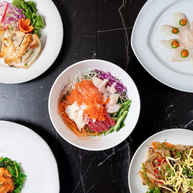 A top-down view of various Japanese dishes, including sashimi, noodles, and grilled fish, on a black marble table.