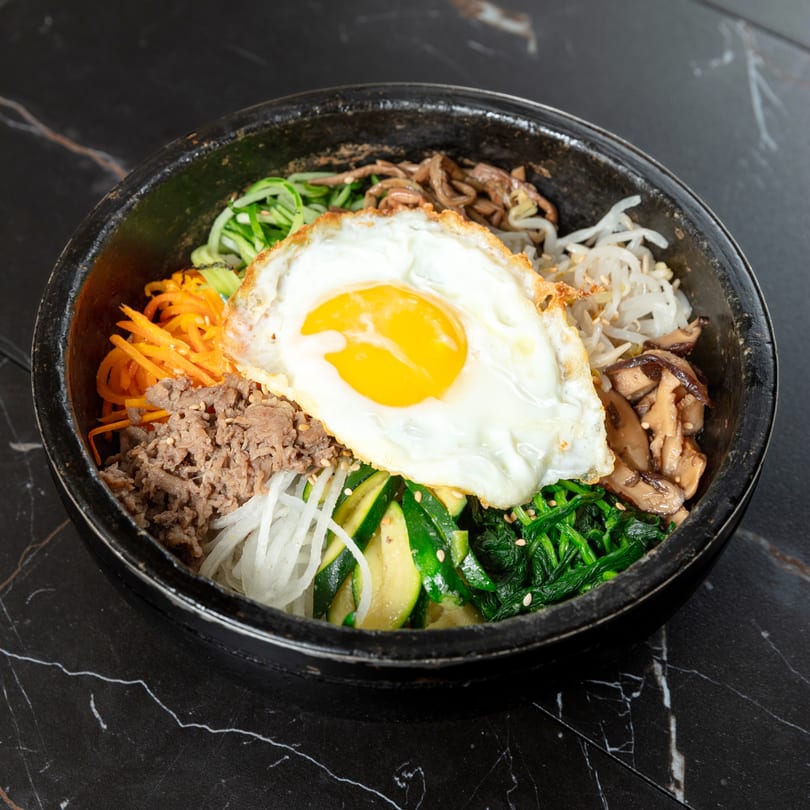 Bibimbap with beef, assorted vegetables, and a fried egg in a black stone bowl.