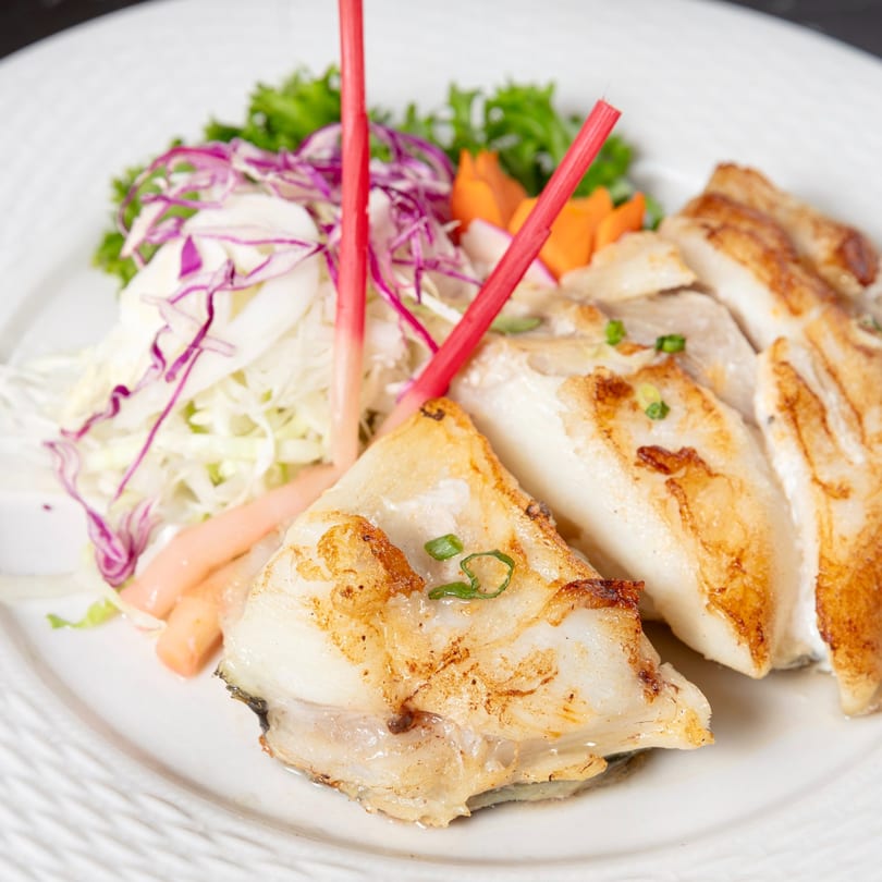 Grilled Japanese fish with red and purple cabbage salad, garnished with red ginger and carrots.