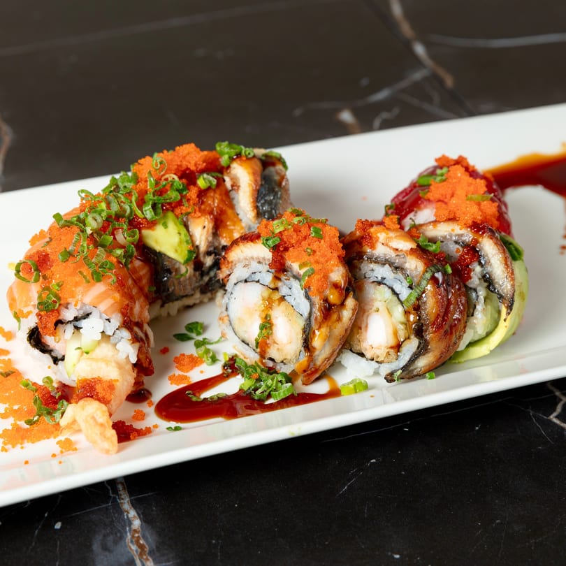 Dragon roll sushi with salmon, eel, avocado, and shrimp tempura, topped with roe and scallions.