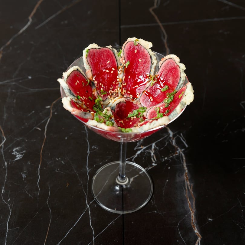 Seared tuna sashimi with sesame seeds and green onions in a martini glass on a black marble table.